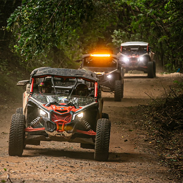 Um comboio com três veículos Can-Am avançando de frente por uma estrada de terra.